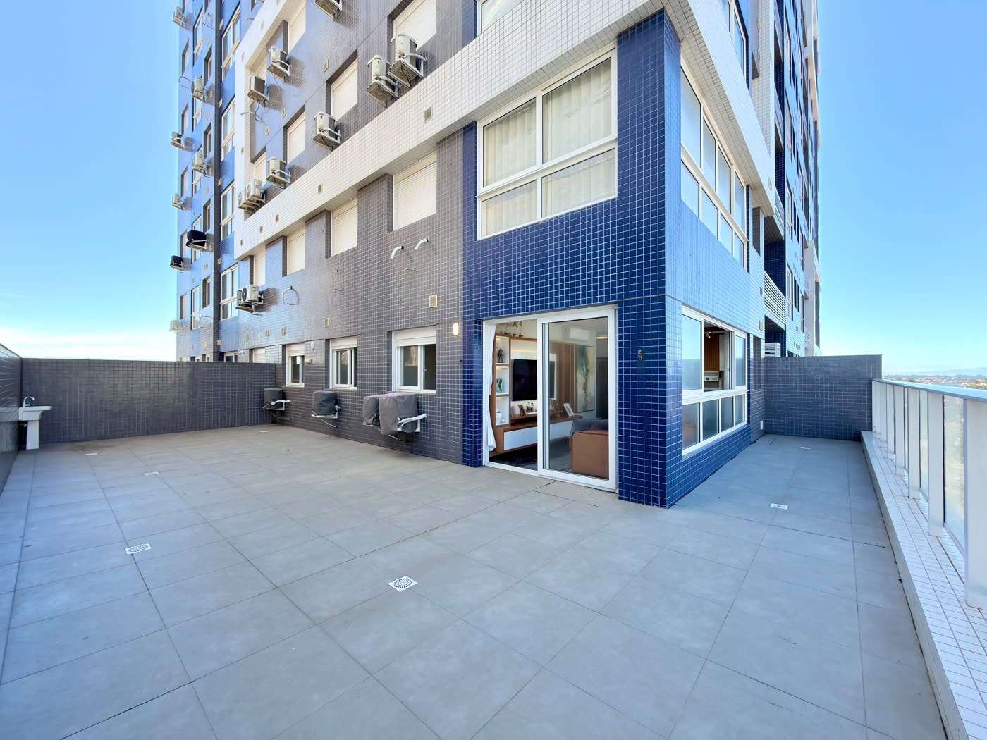 Terraço privativo em L do apartamento 506, com piso claro e guarda-corpo de vidro